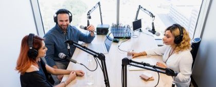 Three podcasters sitting at a desk talking into microphones